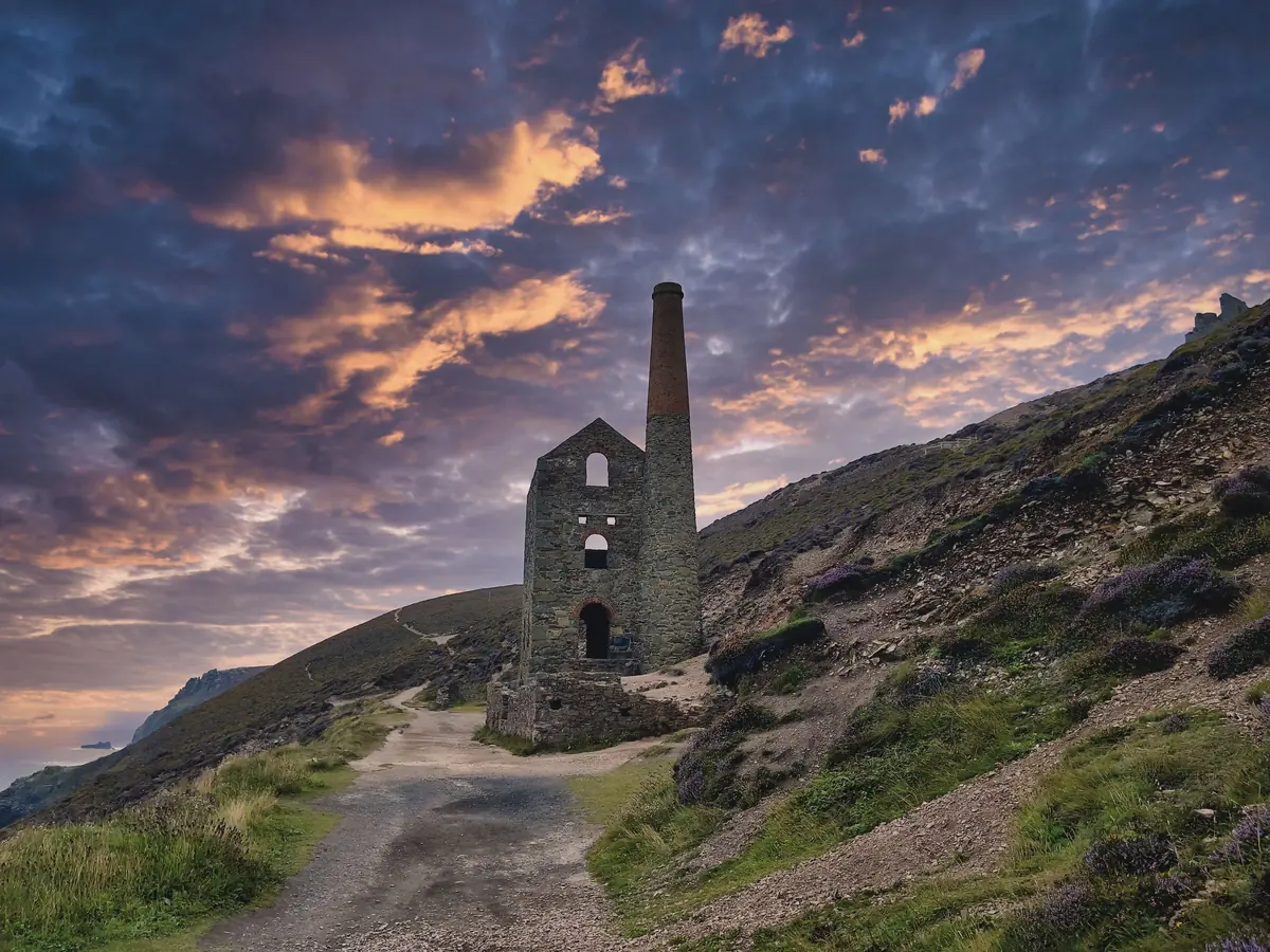 A ruined engine house on a clifftop path under a fiery sunset sky
